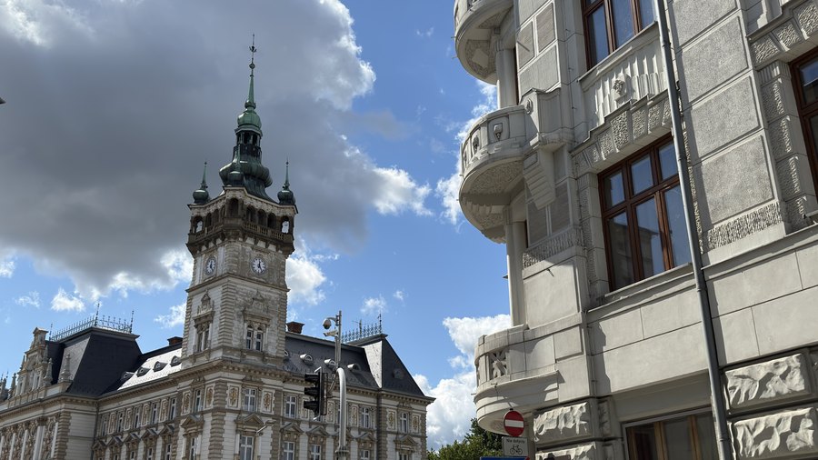 Wieża zegarowa ratusza w Bielsku-Białej na tle chmur, obok narożna kamienica z balkonami