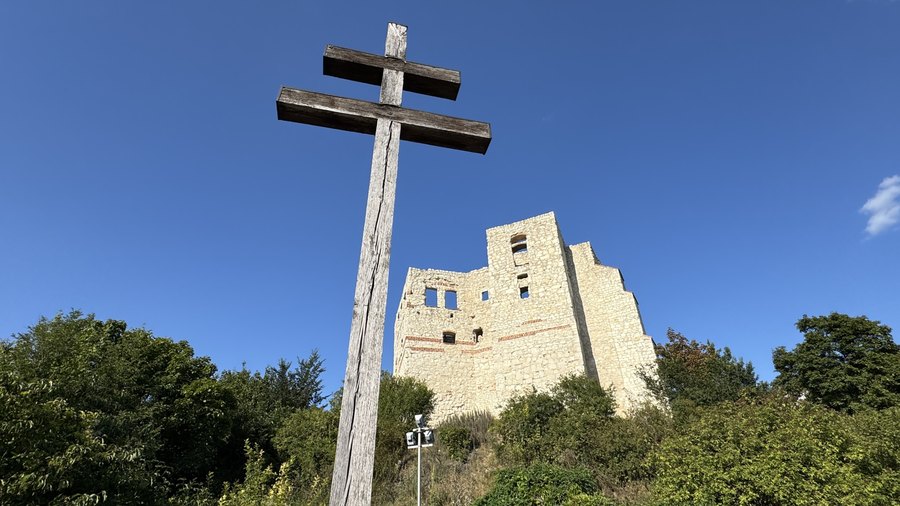 Drewniany krzyż przed ruinami kazimierskiego zamku wśród zieleni