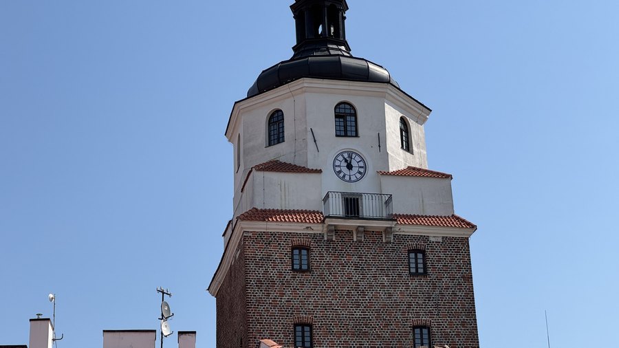 Biała nadbudowa Bramy Krakowskiej z zegarem i balkonem