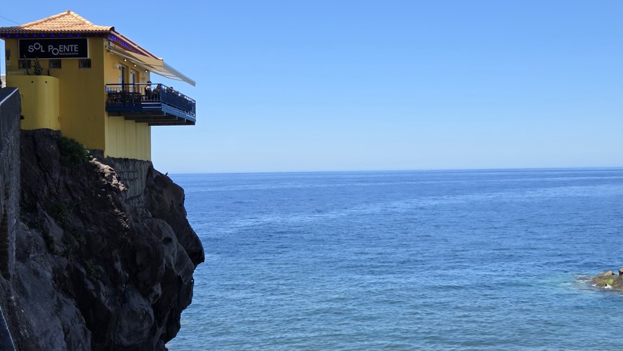 Żółty budynek z tarasem zawieszony na skale nad oceanem w Ponta do Sol
