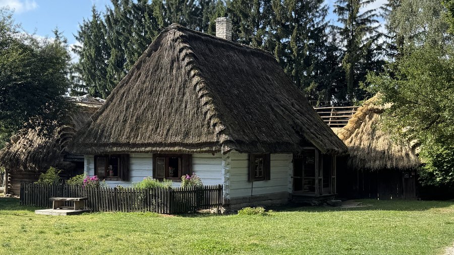 Bielona chałupa kryta strzechą z drewnianym płotem i kwiatami