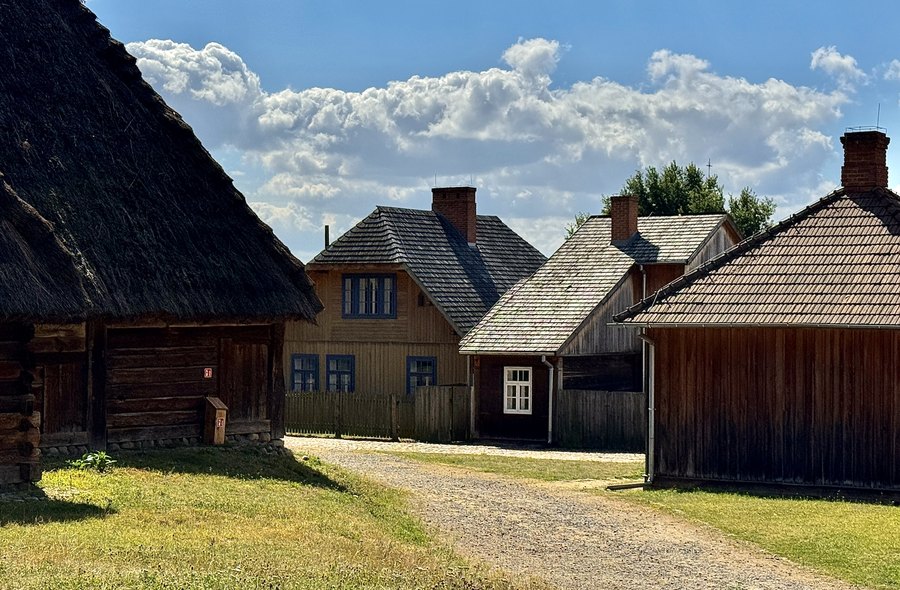 Drewniane zabudowania zagrody przy żwirowej drodze w skansenie